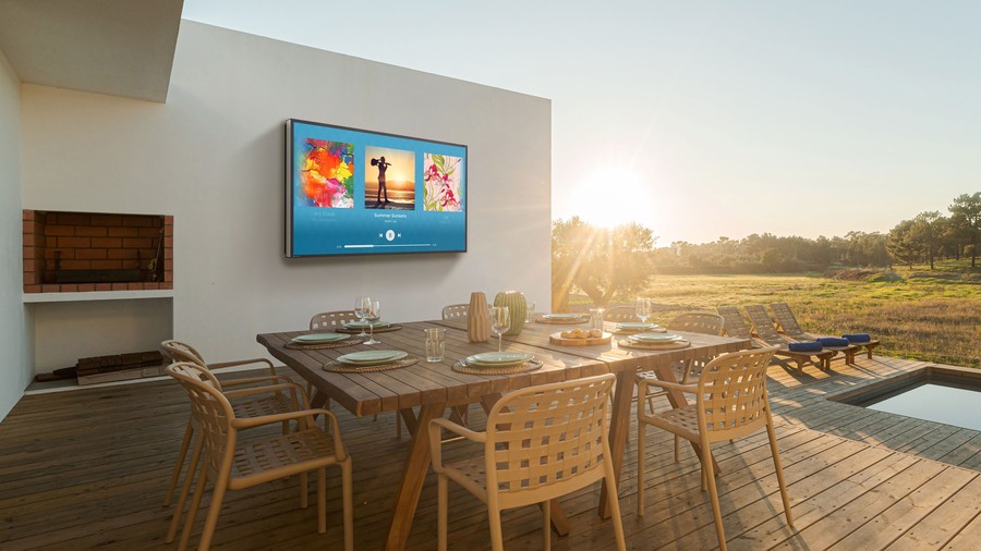 Outdoor dining area by a pool with The Terrace outdoor TV mounted on wall.